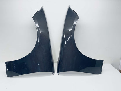 A pair of Carbon Fiber car wheel fenders displayed side-by-side on a white surface against a white wall.