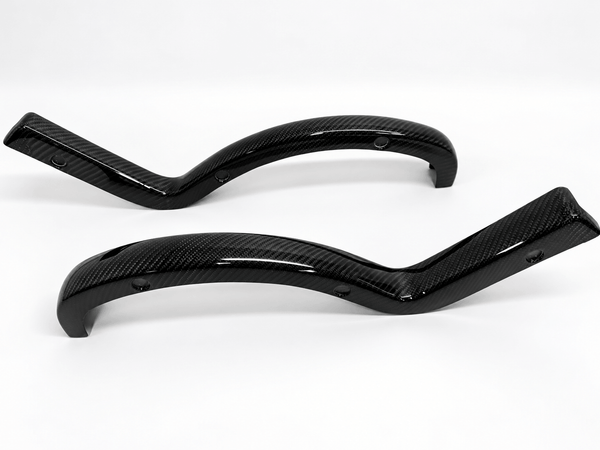 Two glossy black carbon fiber curved trunk arm covers with a visible woven carbon fiber pattern, displayed on a clean white background.