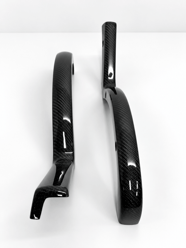 Two glossy black carbon fiber trunk arm covers with a visible woven carbon pattern, displayed on a clean white background.