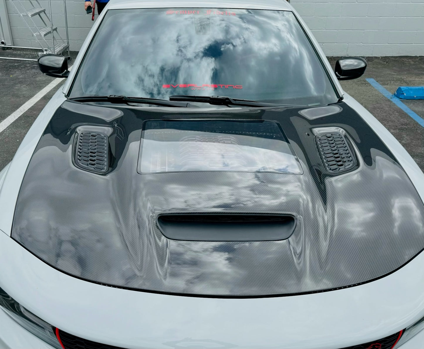 Installed Carbon fiber hood for a Dodge Charger vehicle, featuring a glossy black finish and ventilation slots