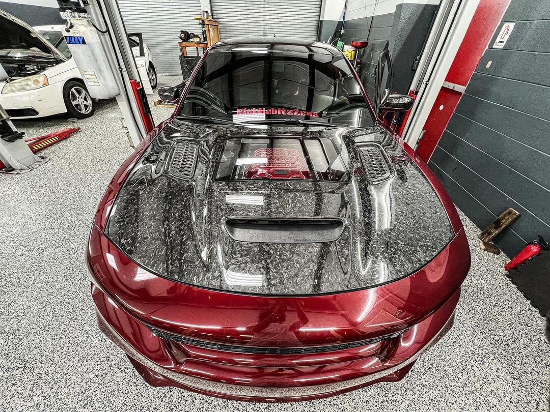 Installed Forged Carbon fiber hood for a Dodge Charger vehicle, featuring a glossy finish and ventilation slots